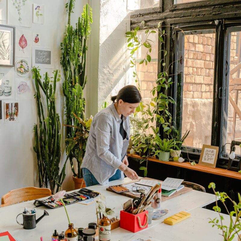 woman working on an art piece surrounded by art and plants in her apartment